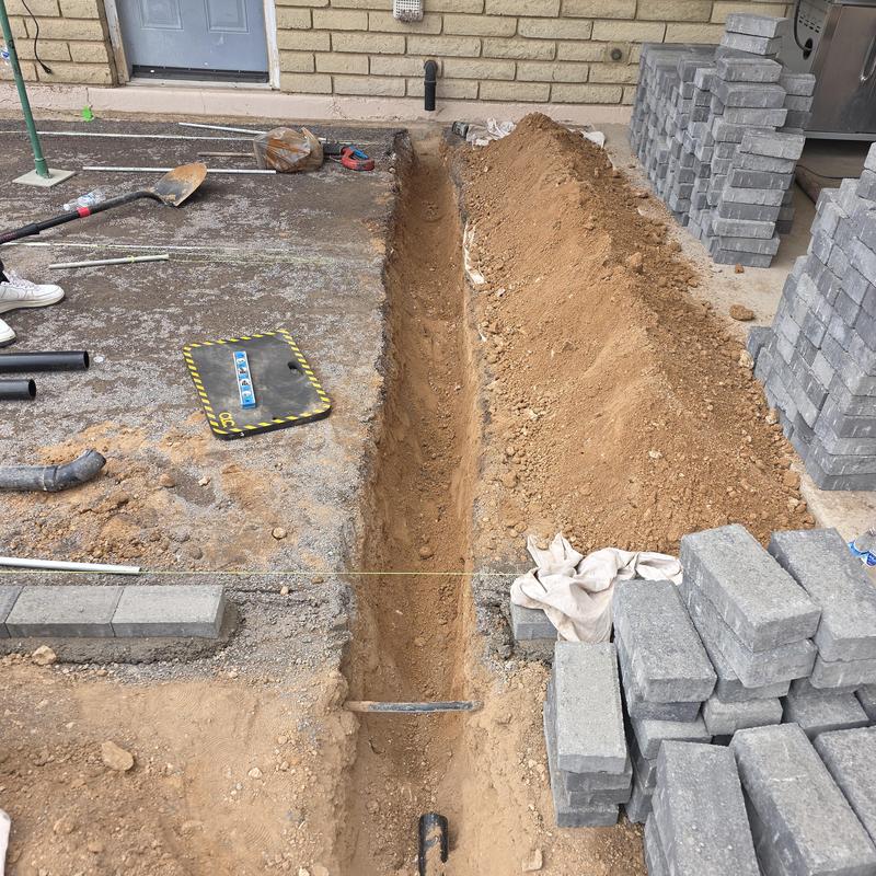 Kitchen drain piping trench with pavers stacked nearby