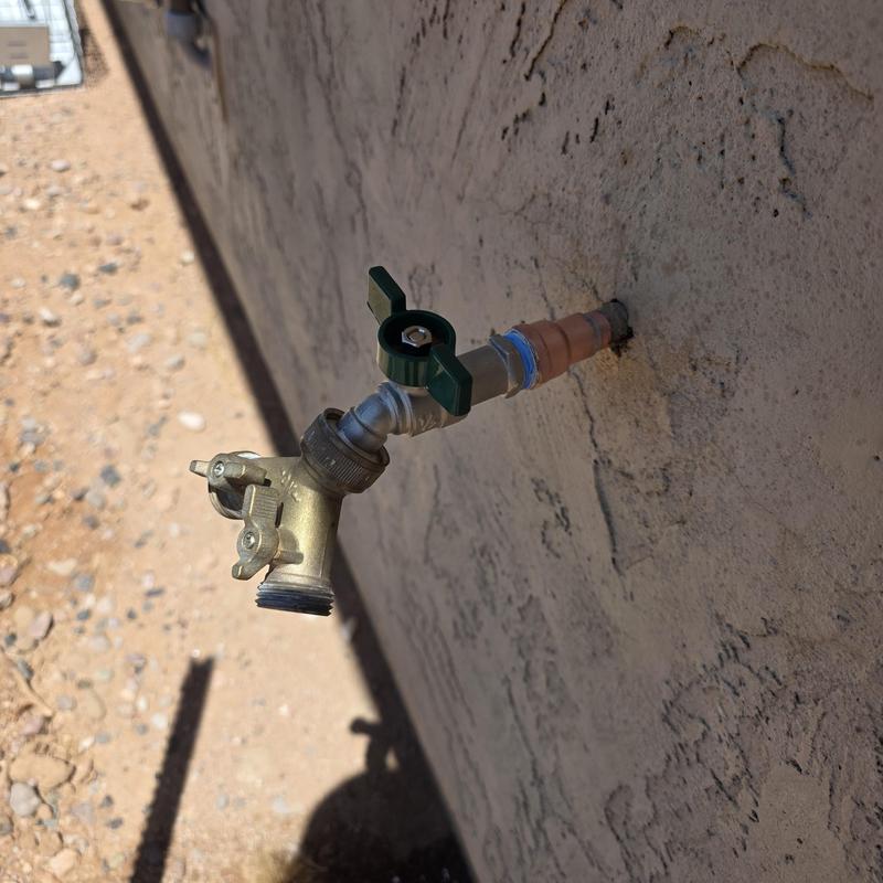 Outdoor hose bib with green valve handle on stucco wall
